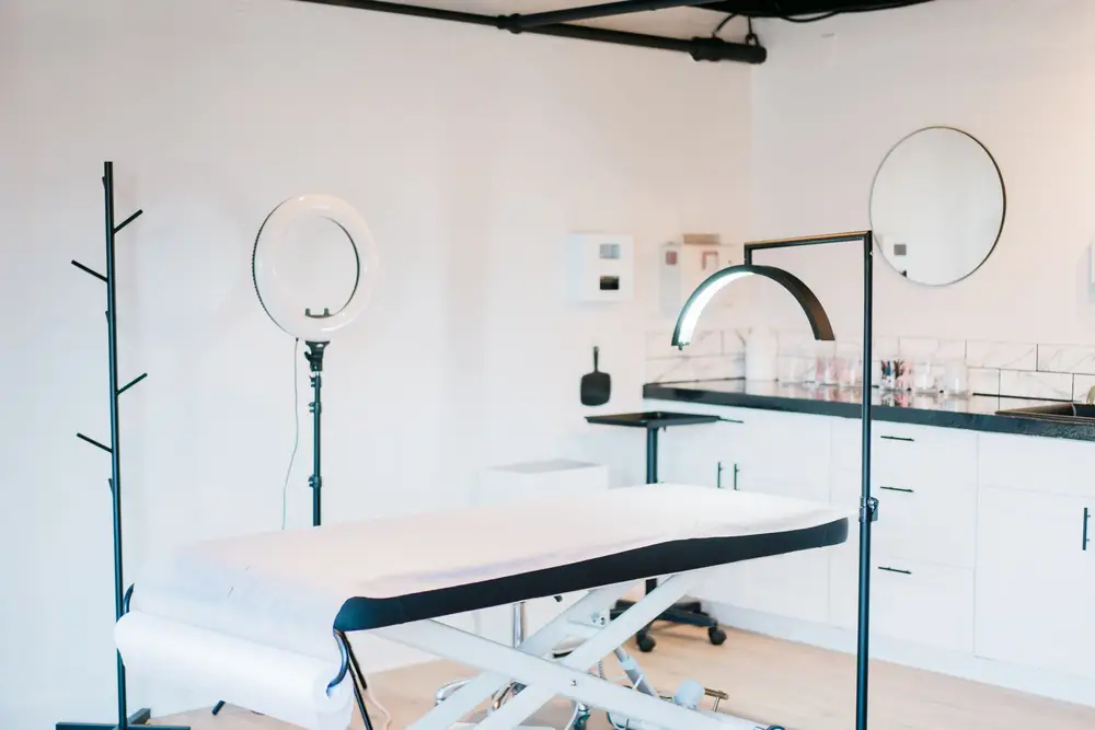 A bright, minimal treatment room with a treatment bed and ring light